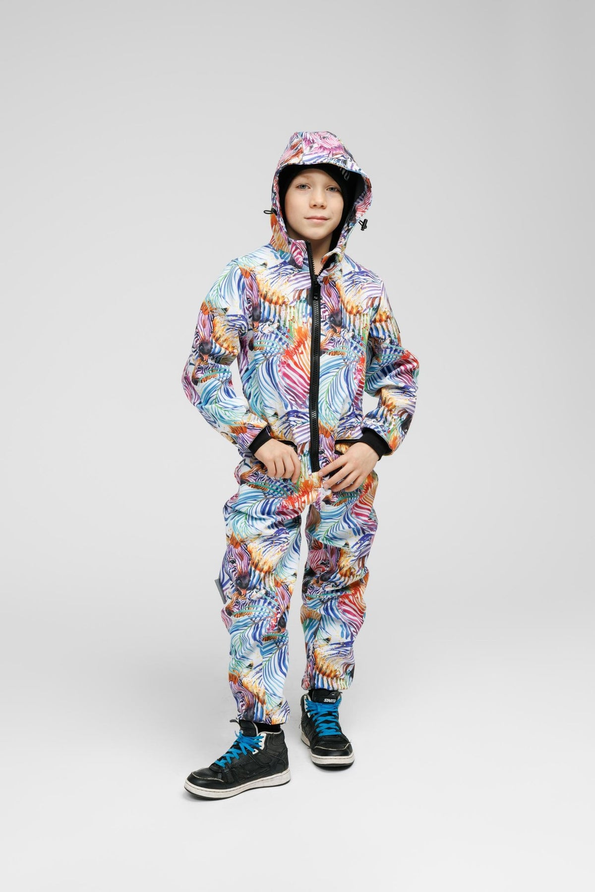 7. Child in Nuckö rainbow softshell onesie with hood, hands in pockets, studio setting