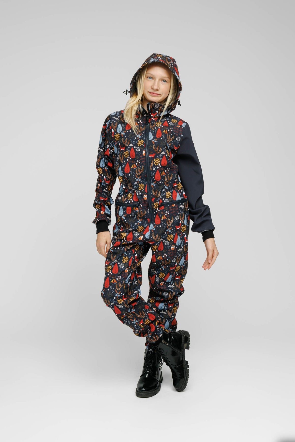8. Child wearing Nuckö softshell onesie with forest print, standing with hood up in studio