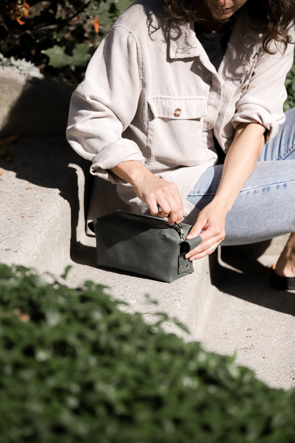 9. Woman opening eleriinseim leather cosmetic bag in Forest color on steps