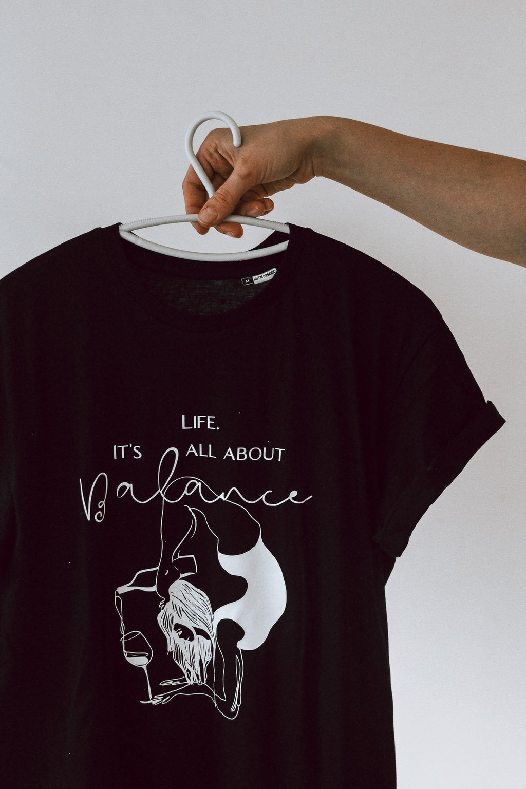 6. Black 'It's All About Balance' T-shirt by Black Giraffe Brand on hanger, showcasing design and rolled-up sleeves