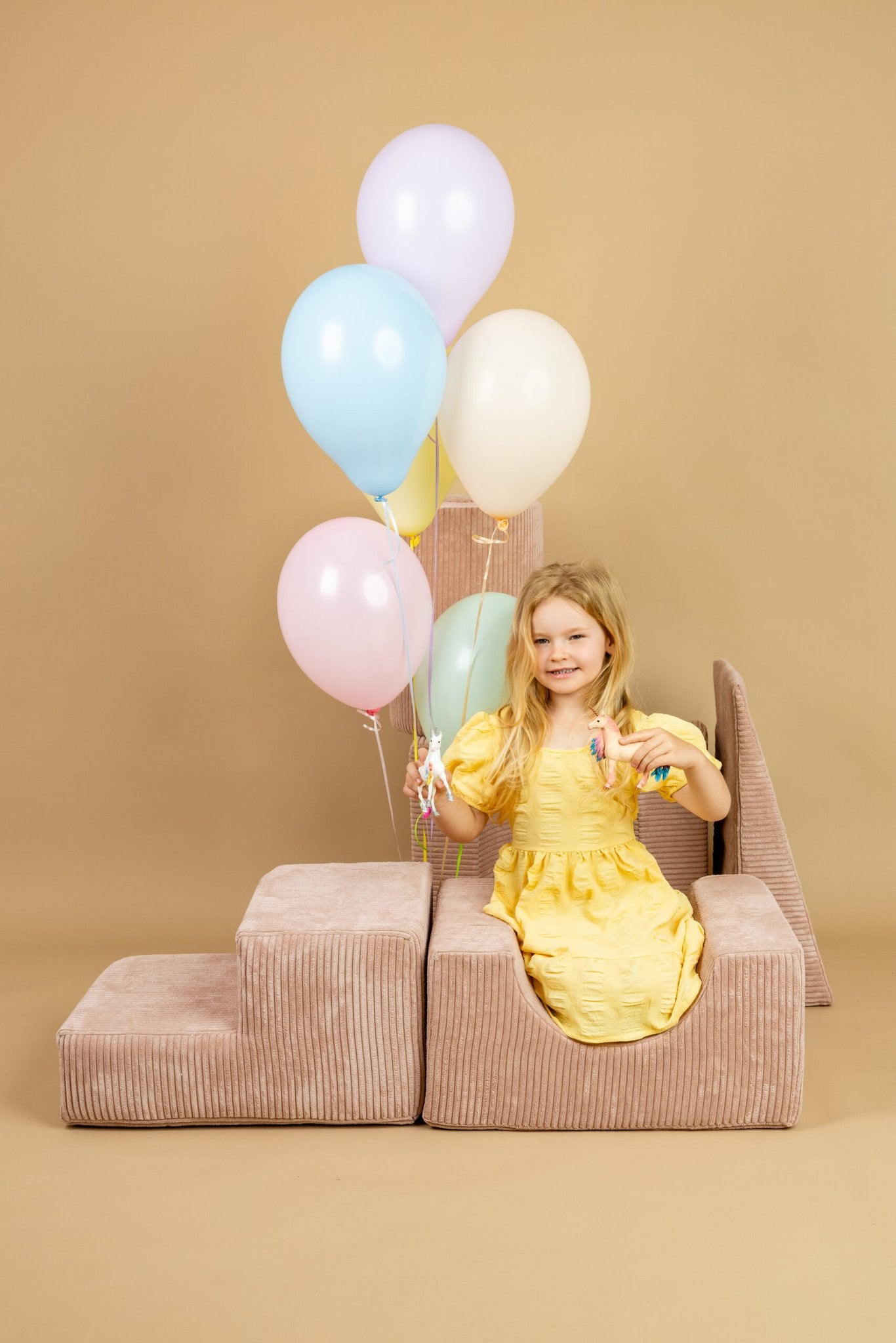 1. Girl in yellow dress enjoying powder pink shape set, surrounded by colorful balloons, in a playful indoor scene