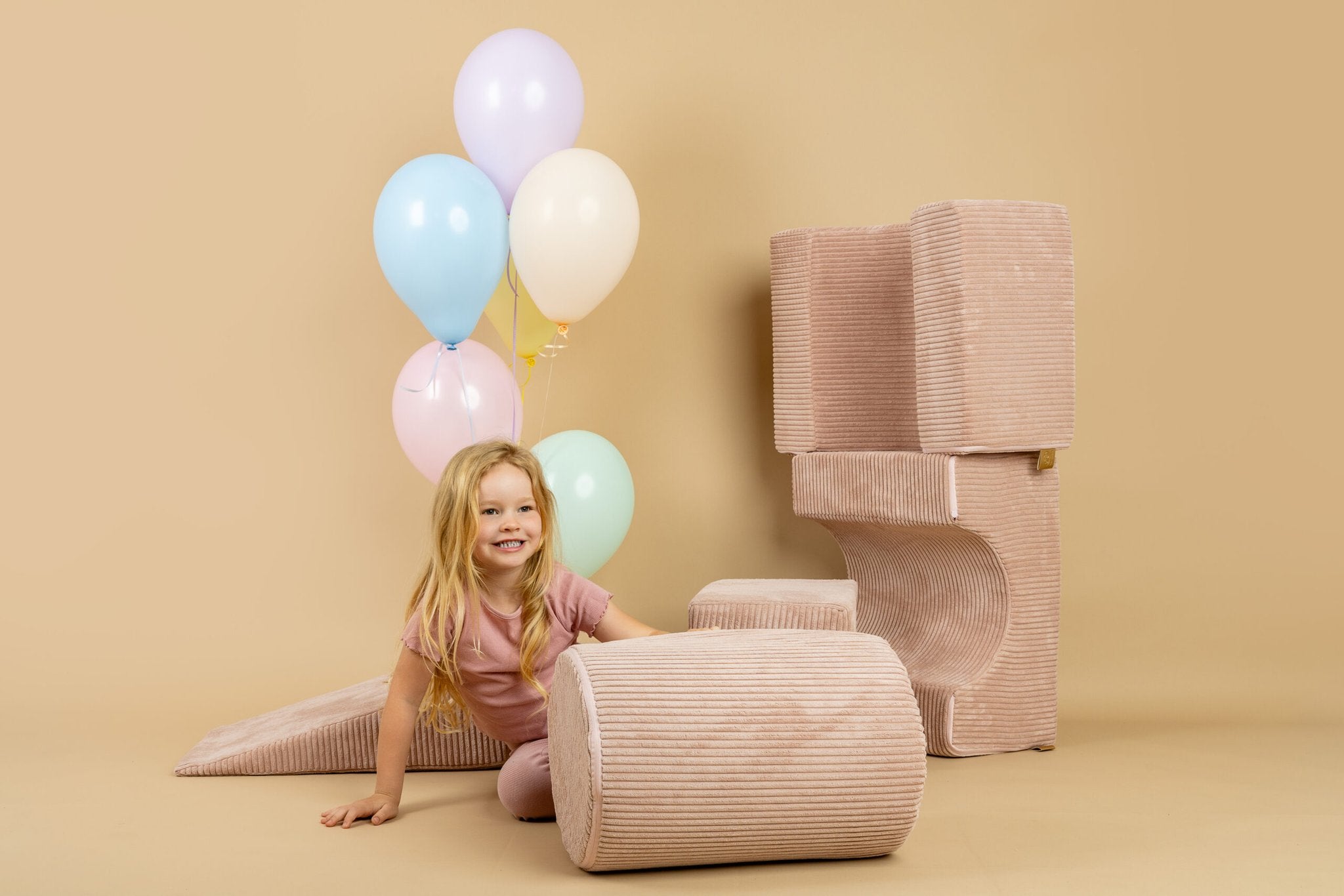 1. Girl in pink outfit playing with powder pink shape set and balloons in a beige room