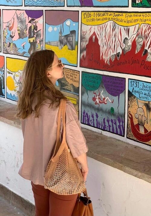 4. Woman with brown hair wearing sunglasses, holding a beige VÕRK organic cotton string bag by Sidrunid, standing in front of colorful mural