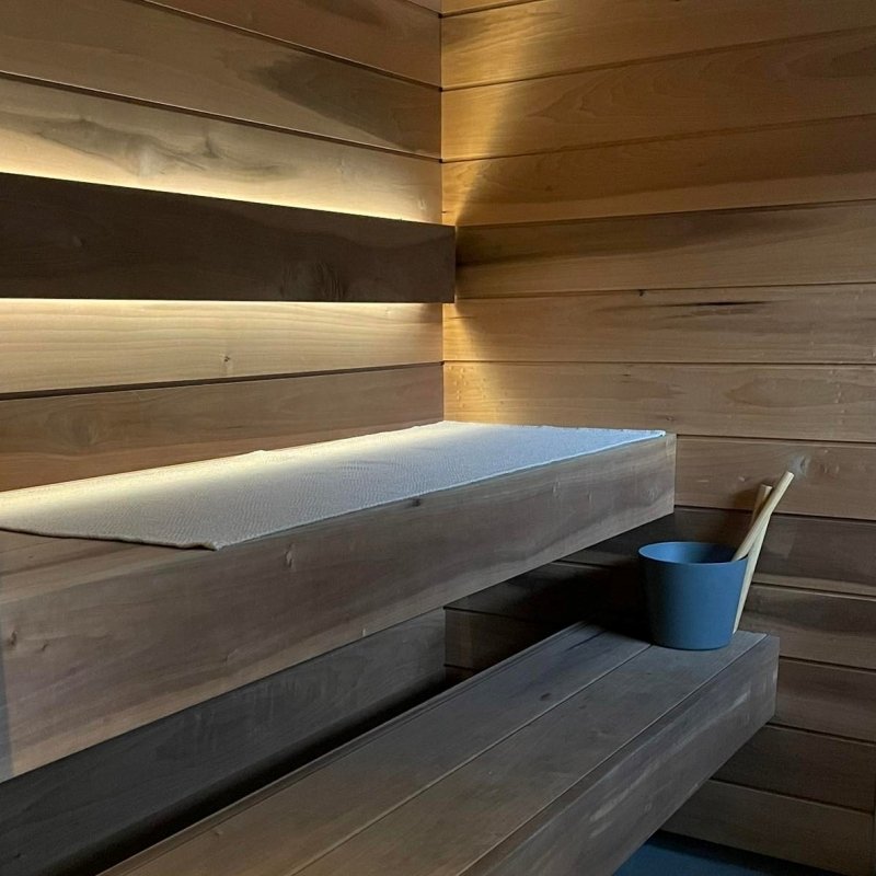 1. Beige linen sauna seat cover on upper wooden bench in a dimly lit sauna with wooden walls and a bucket