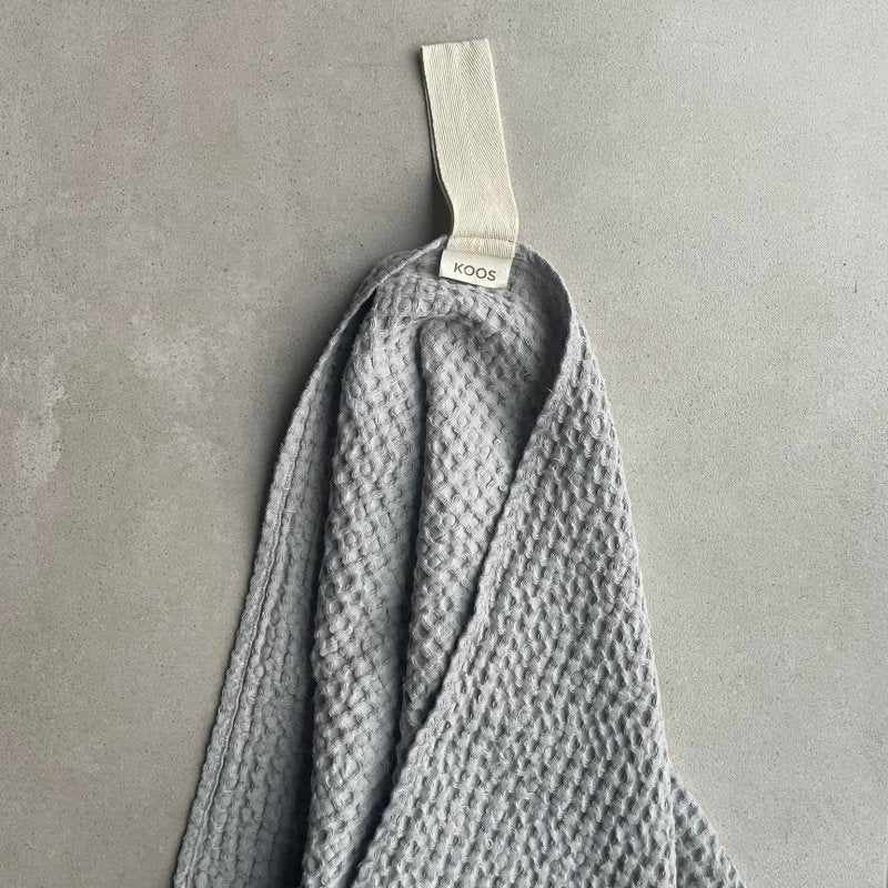 1. Gray waffle fabric towel with white cotton hanger on concrete background, featuring KOOSdisain label