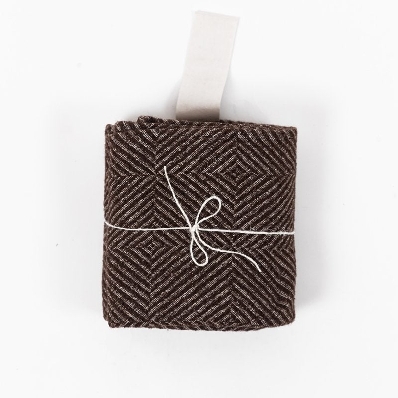 3. Rolled brown linen towel with checkered fishbone pattern tied with string and white cotton hanger on white background