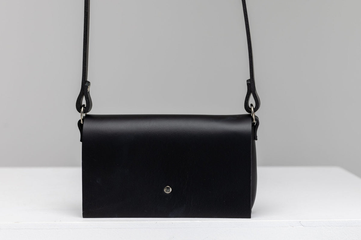 3. Studio shot of PYKOK KORA minibag in black leather with magnetic closure, displayed on white surface