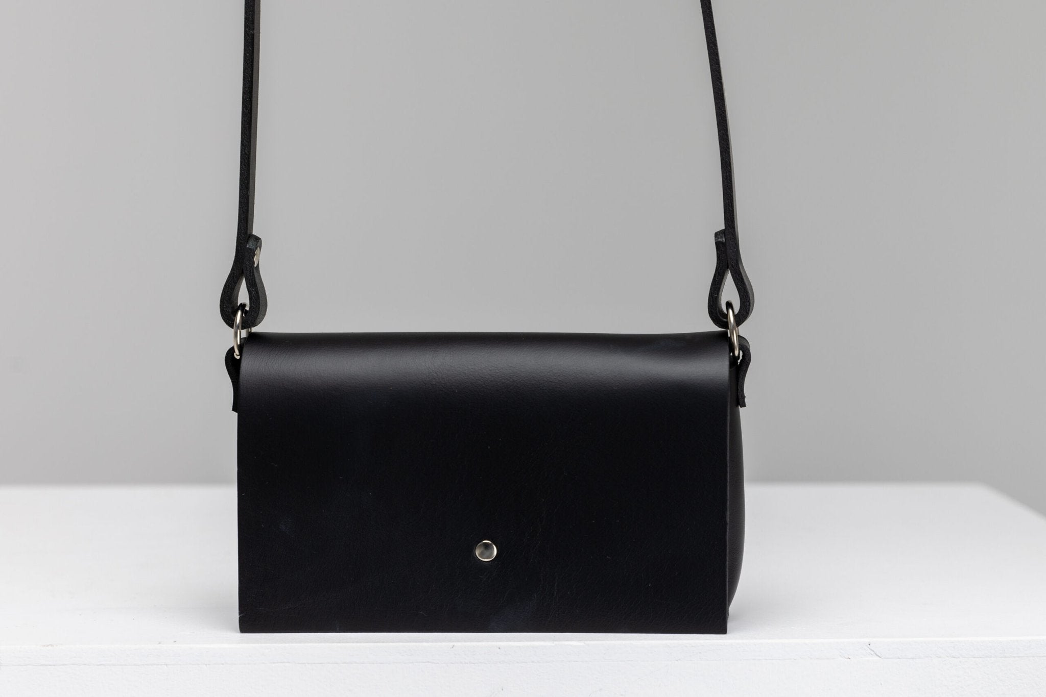 3. Studio shot of PYKOK KORA minibag in black leather with magnetic closure, displayed on white surface