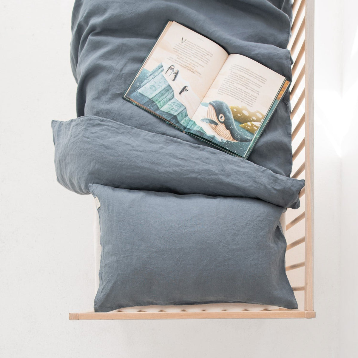 1. Overhead view of kids' bed with blue fog linen duvet cover and open book, in a bright nursery