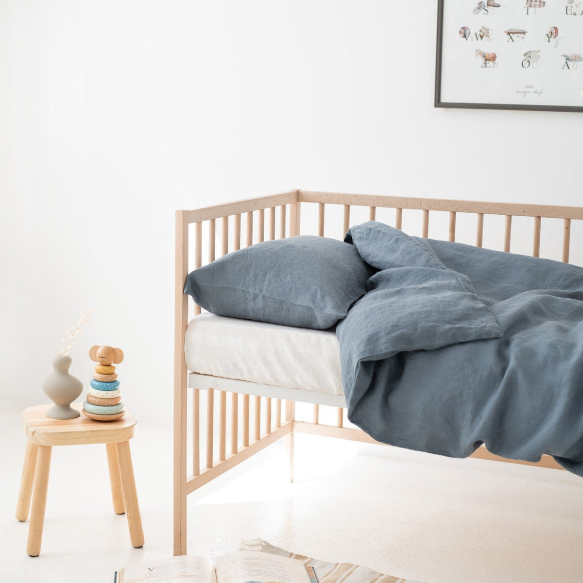 1. Kids' bed with blue fog linen duvet cover set in a bright room, featuring a wooden crib and decorative items