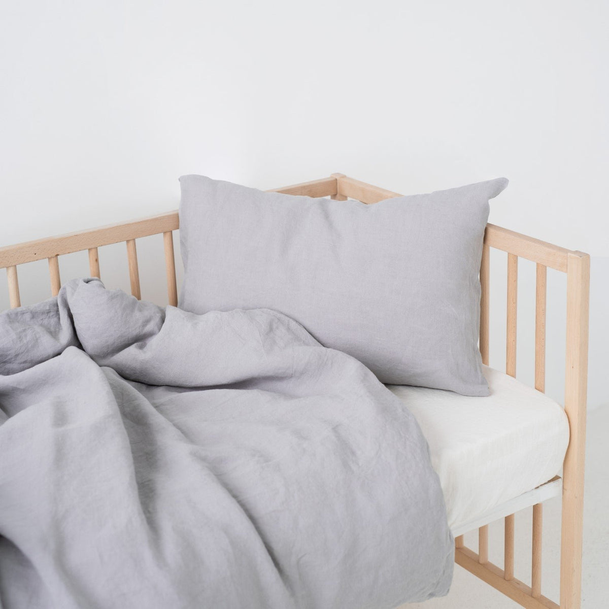 2. Light grey linen duvet cover set on a crib, showcasing the pillow and duvet arrangement in a simple setting