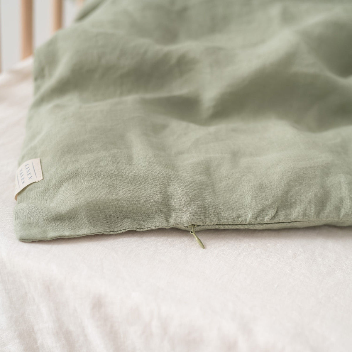 12. Close-up of sage green linen duvet cover with zipper detail on white bed