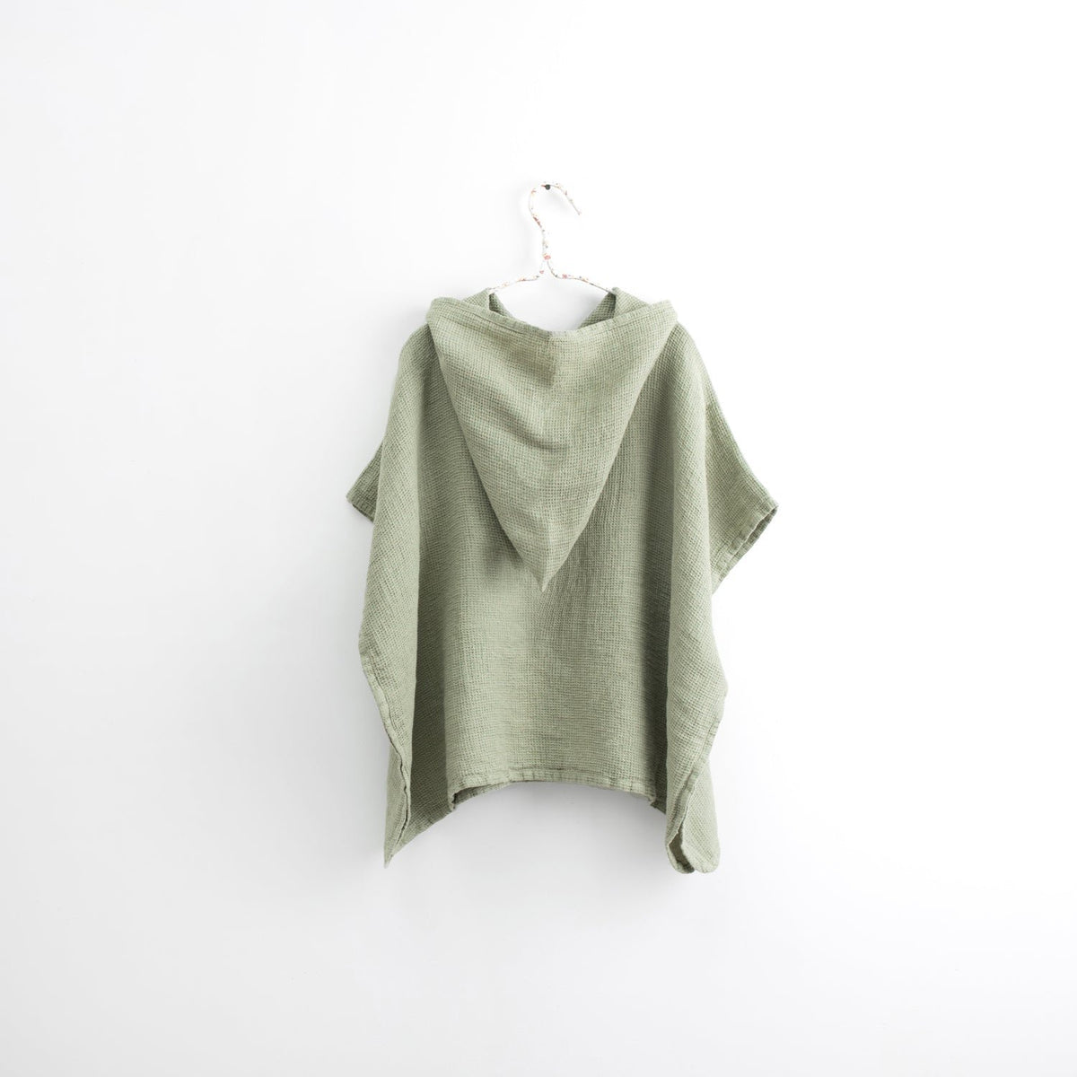 2. Back view of kids' sage green linen poncho with hood on white background, highlighting fabric drape