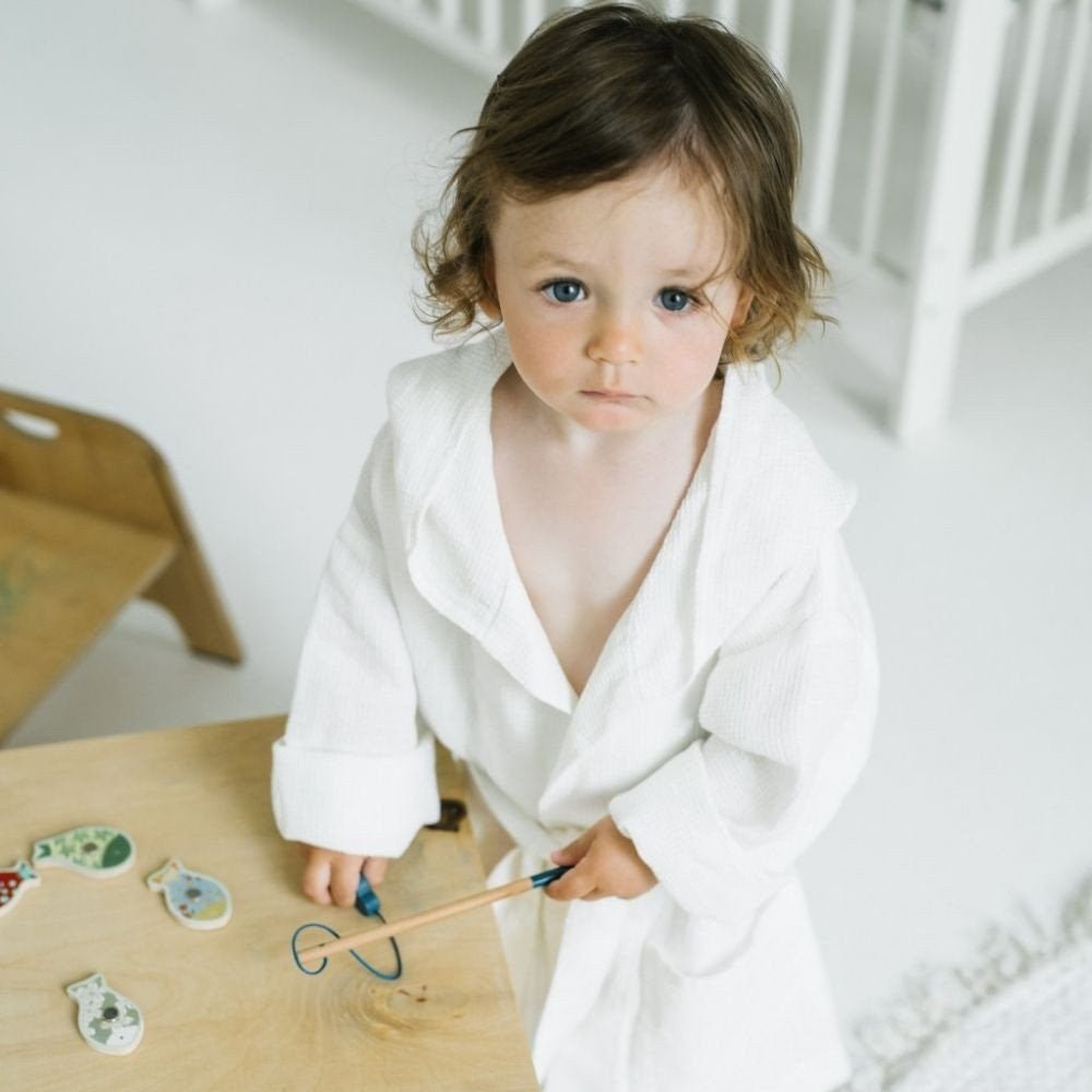1. Child wearing white linen bathrobe with hood, playing with toys in a bright room