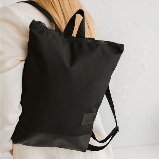 2. Woman wearing Muni black leather bottom backpack, highlighting waterproof polyester material and urban style