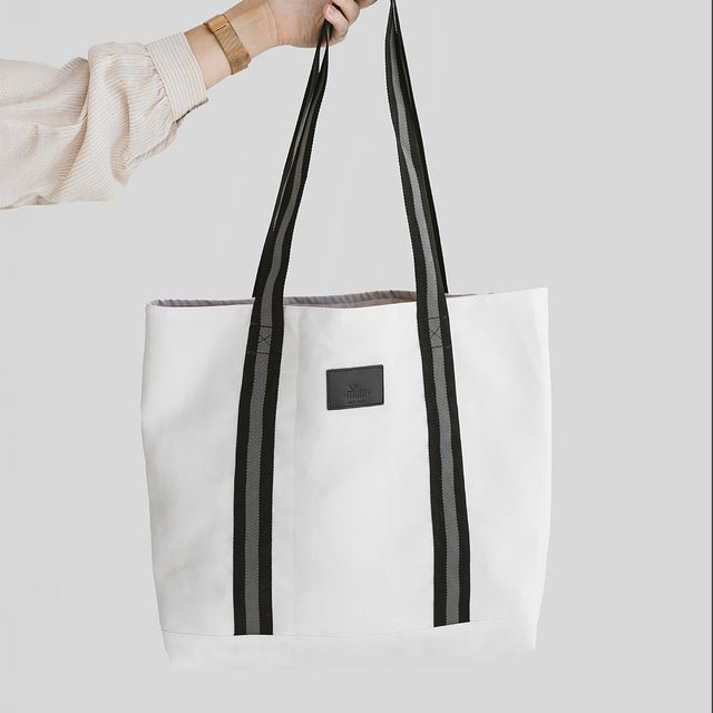 3. Close-up of Muni white denim tote bag with black straps, held by a hand