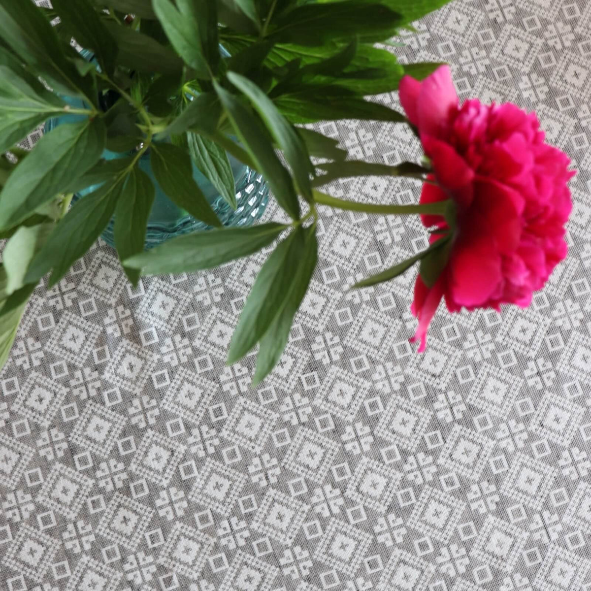 3. Overhead view of LOKO Tartumaa tablecloth displaying Kodavere folk art pattern, with a focus on the intricate design and a red flower in a blue vase