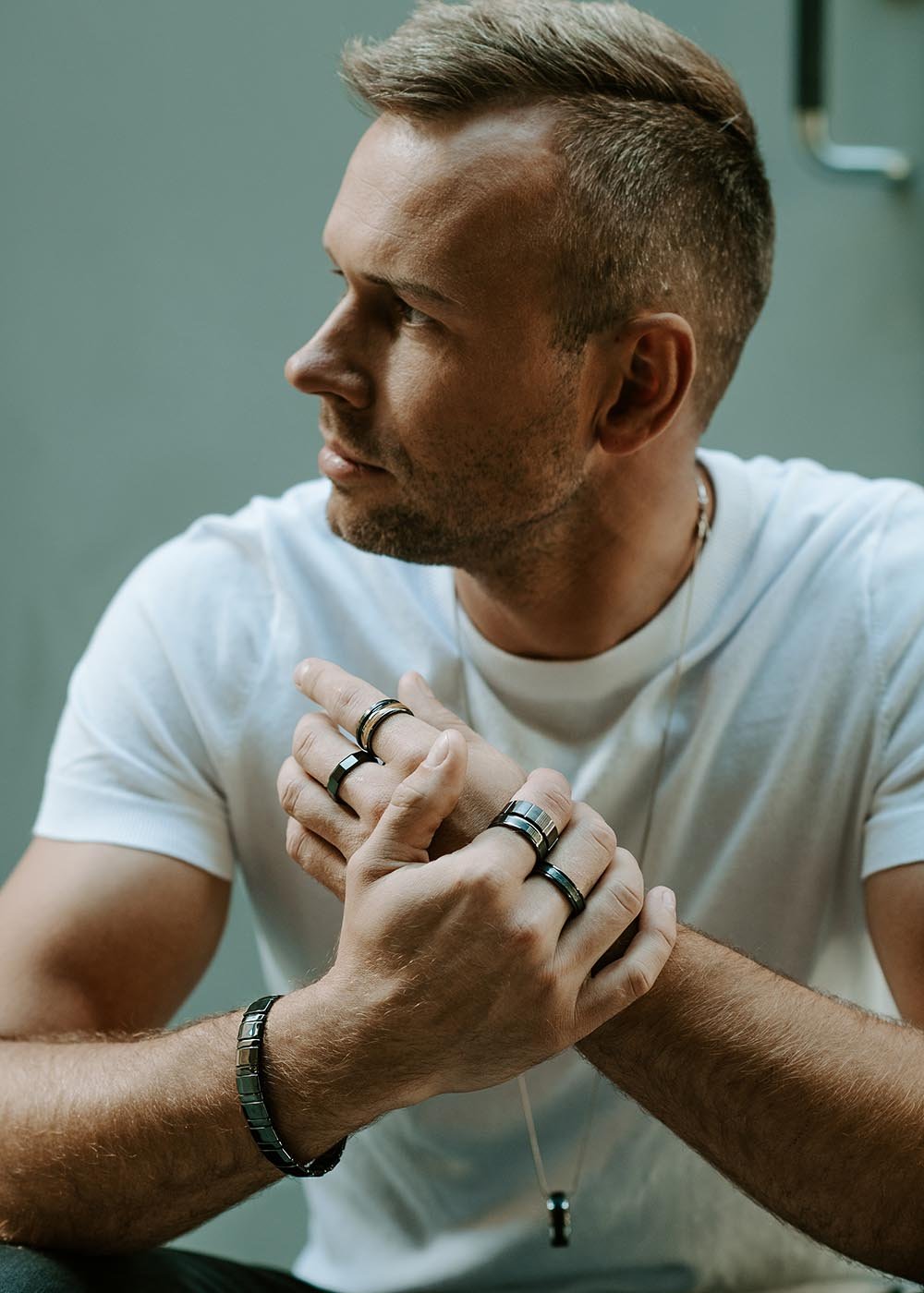 1. Man wearing multiple Leomani rings and bracelet, dressed in a white t-shirt, sitting in a casual setting