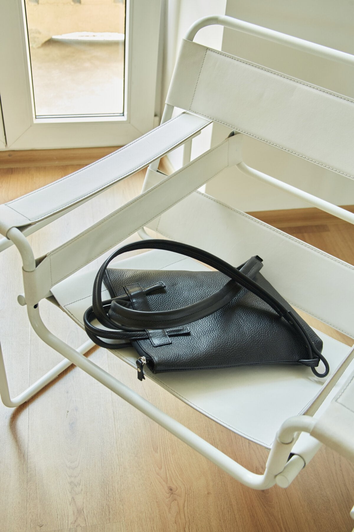 4. Lava Flow ALICE ARM black leather backpack on chair, displaying straps and secure zippered closure