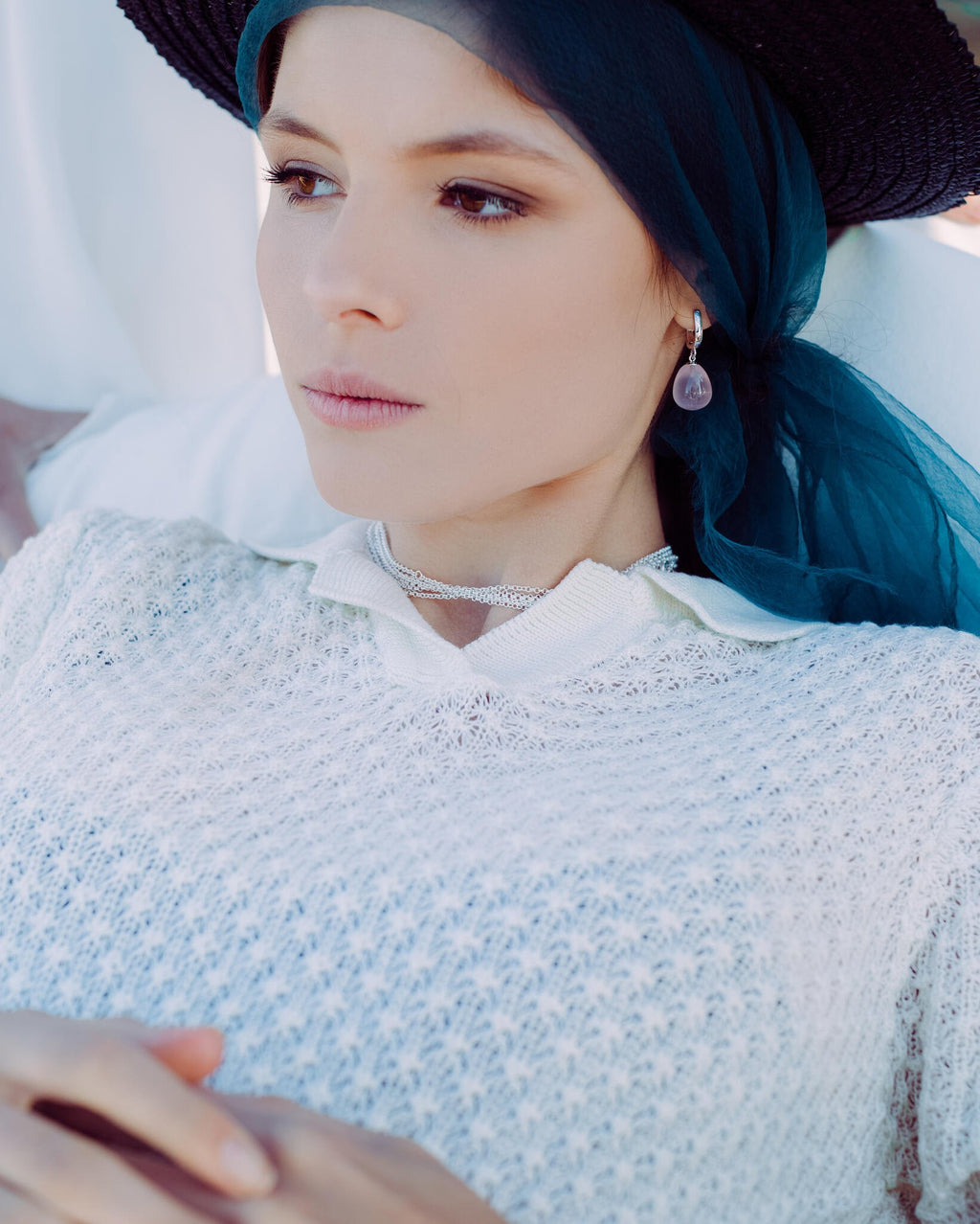 1. Woman wearing rose quartz earring with blue headscarf and white knit top, lying down