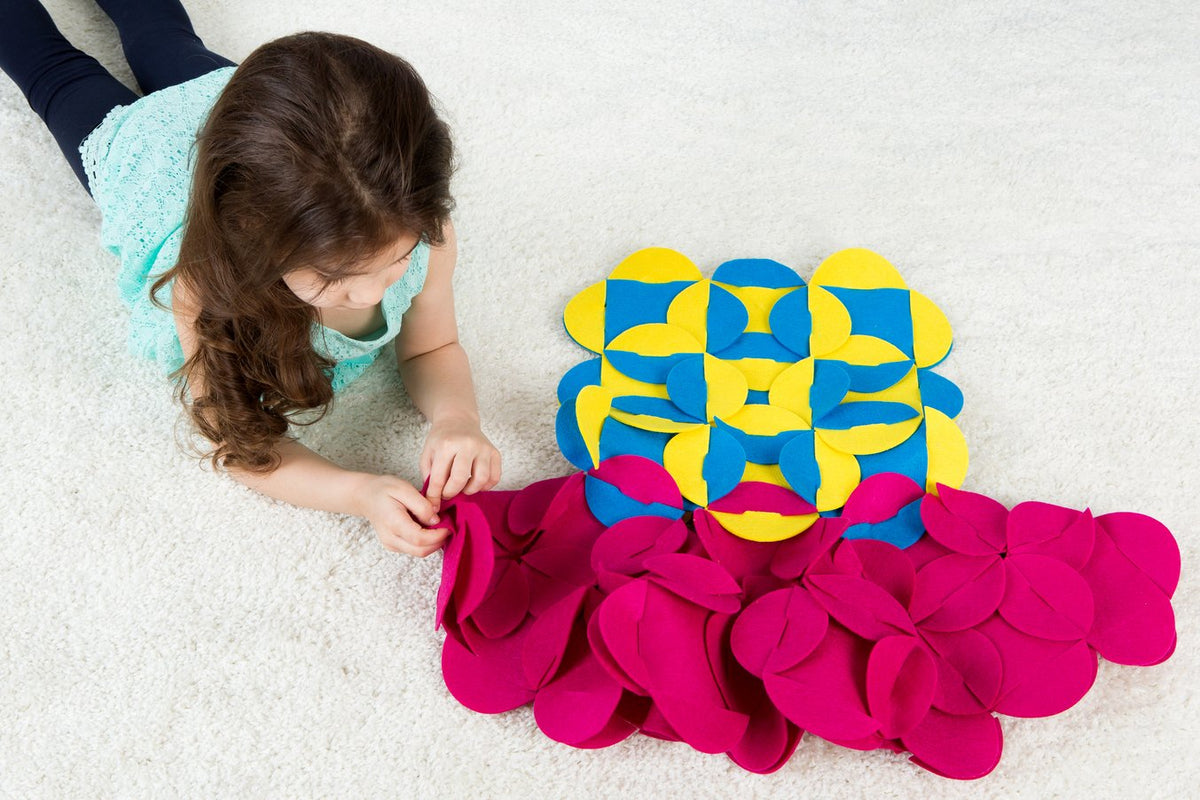 7. Girl lying on carpet assembling pink and blue felt pieces into a costume