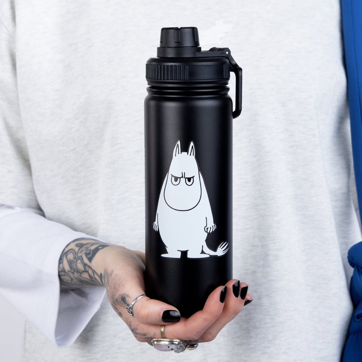 1. Moomintroll Thermal Everyday Bottle held by a person, showcasing black stainless steel design with Moomin print
