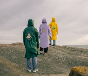 2. Unisex Moomin Adventure Rain Jackets in dark green, purple, and yellow worn by three models on rocky terrain