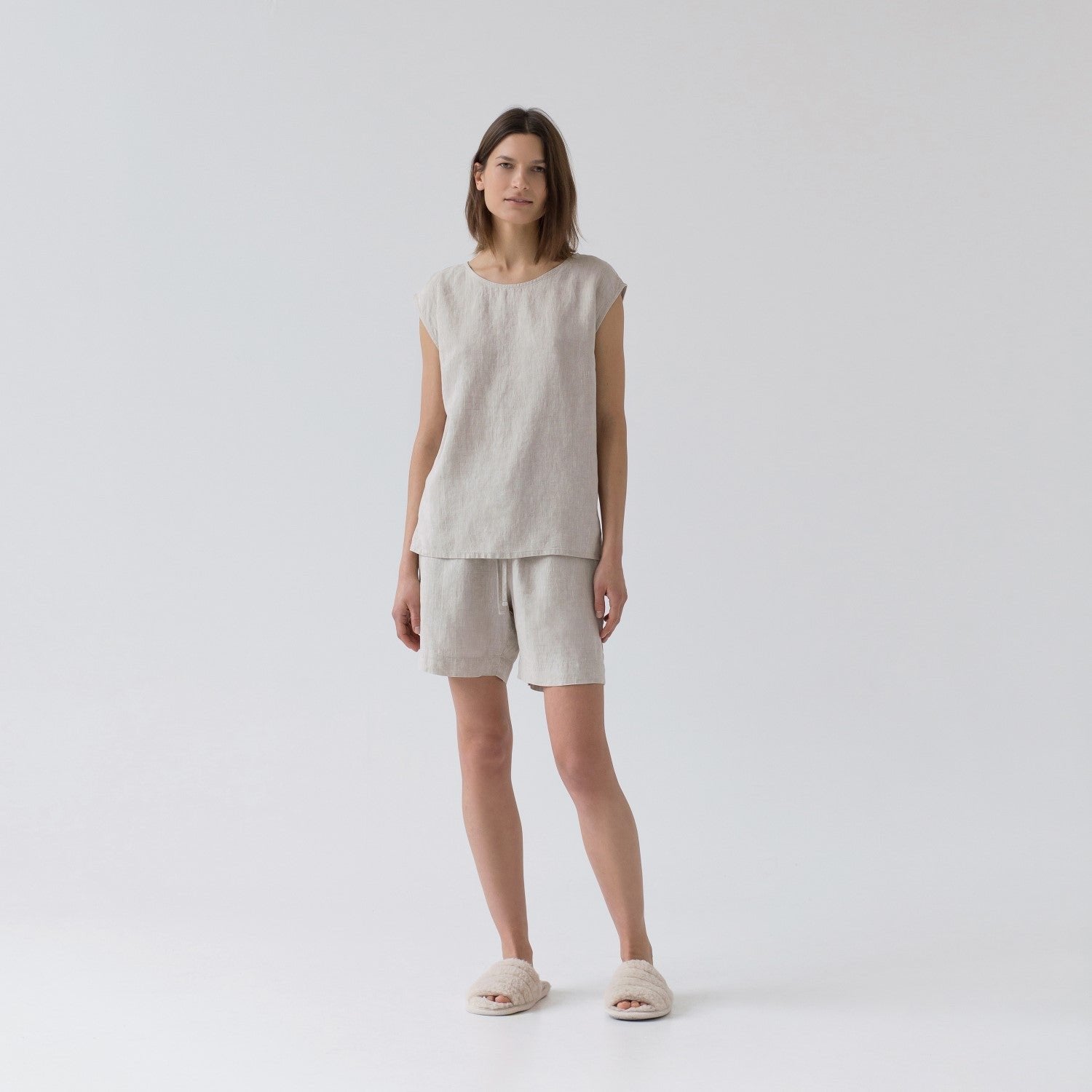 2. Woman in sleeveless beige linen pyjama set with relaxed fit, standing front-facing in a studio setting