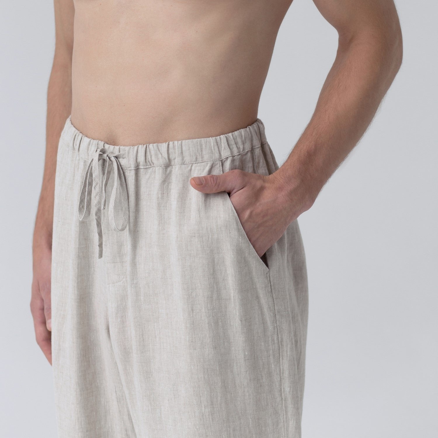3. Close-up of beige linen trousers with elasticated waistband and drawstring, hand in pocket