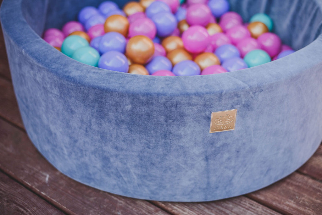 2. Close-up of blue velvet MeowBaby ball pit filled with gold, pink, lilac, and turquoise balls