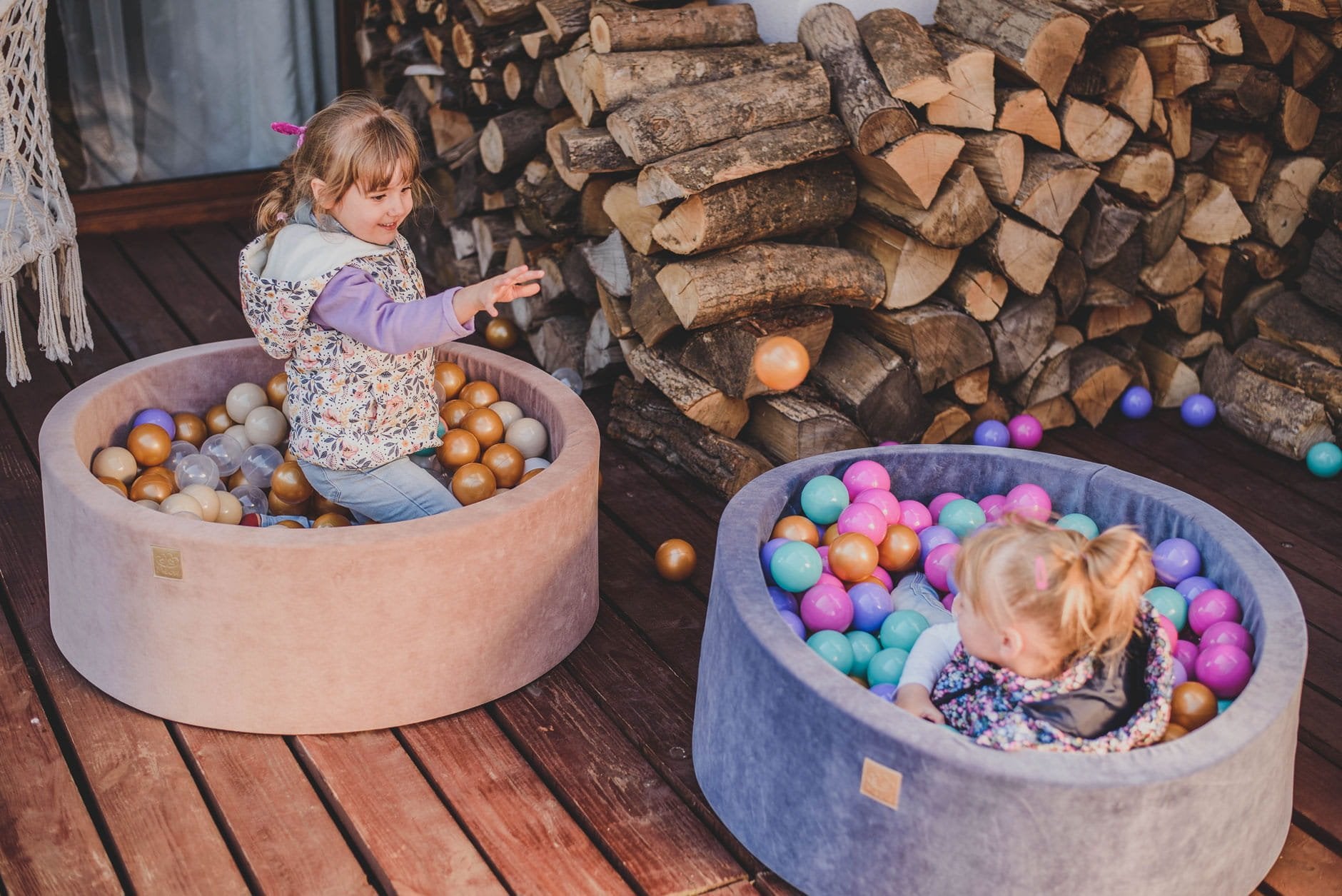 3. Two children playing in MeowBaby ball pits on a wooden deck, one in blue and one in beige