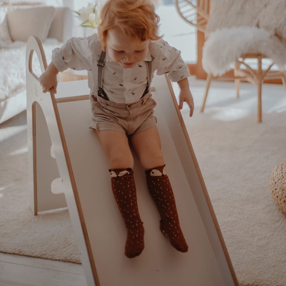 1. Toddler sliding down a white wooden slide in a bright living room