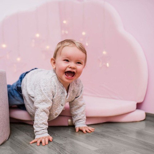 4. Smiling child crawling on a pink cloud-shaped velvet play mat with fairy lights in a cozy room