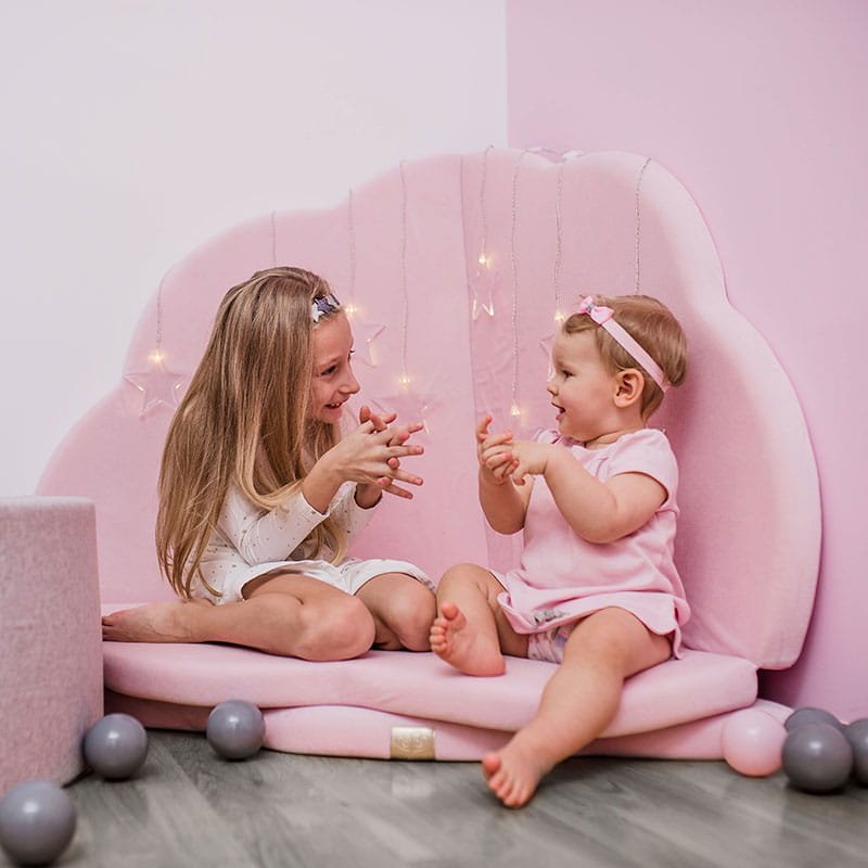 1. Two children playing on a pink cloud-shaped velvet play mat with fairy lights in a cozy room