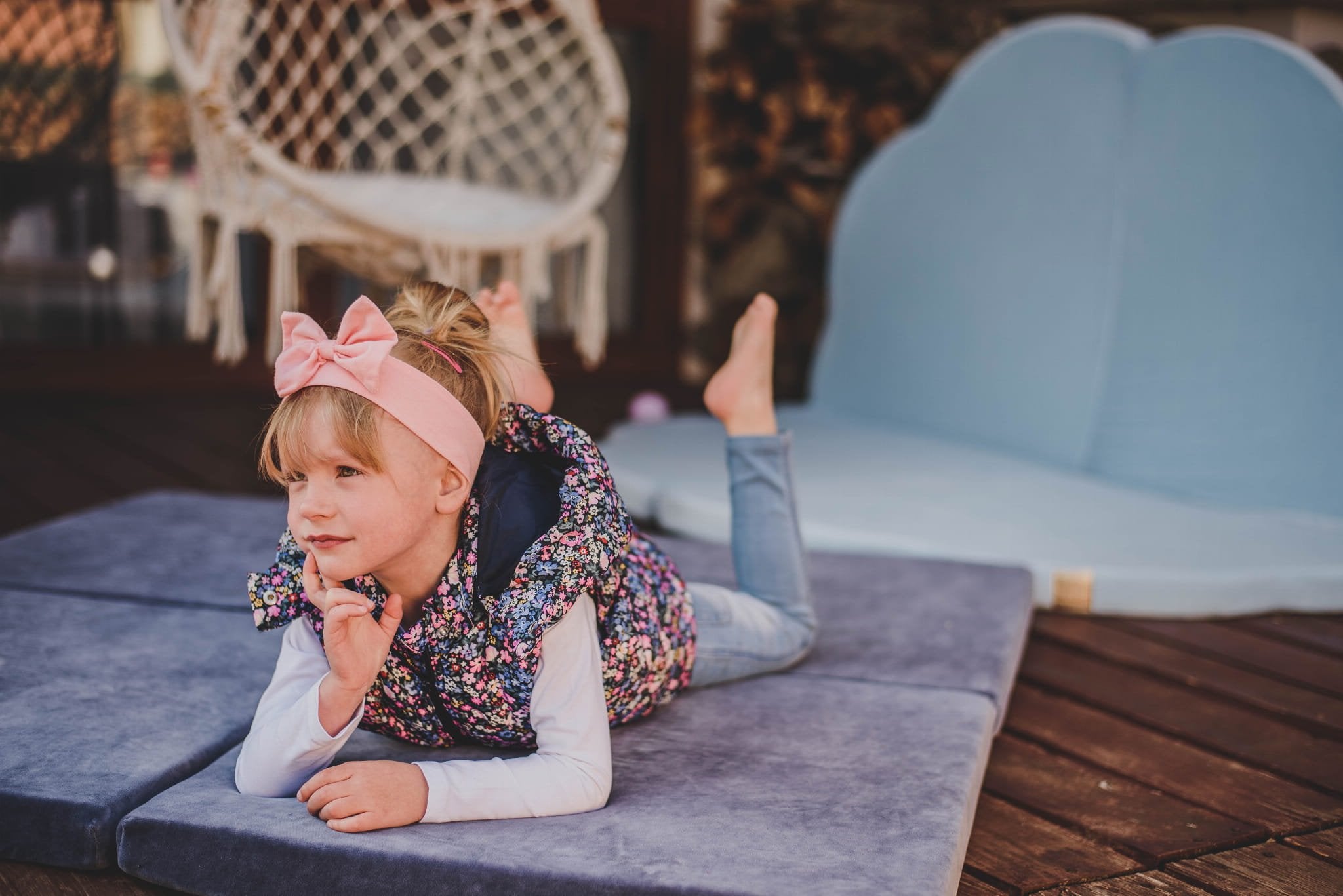5. Child lying on a blue-grey velvet play mat outdoors, wearing a floral vest and pink headband