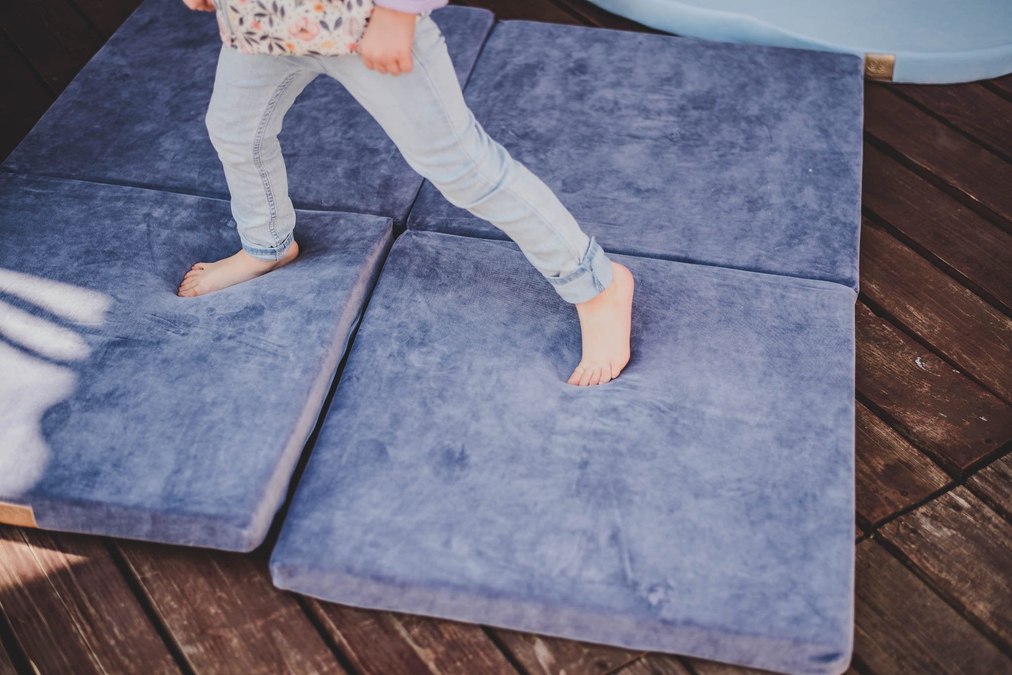 4. Child walking barefoot on a blue-grey velvet play mat outdoors