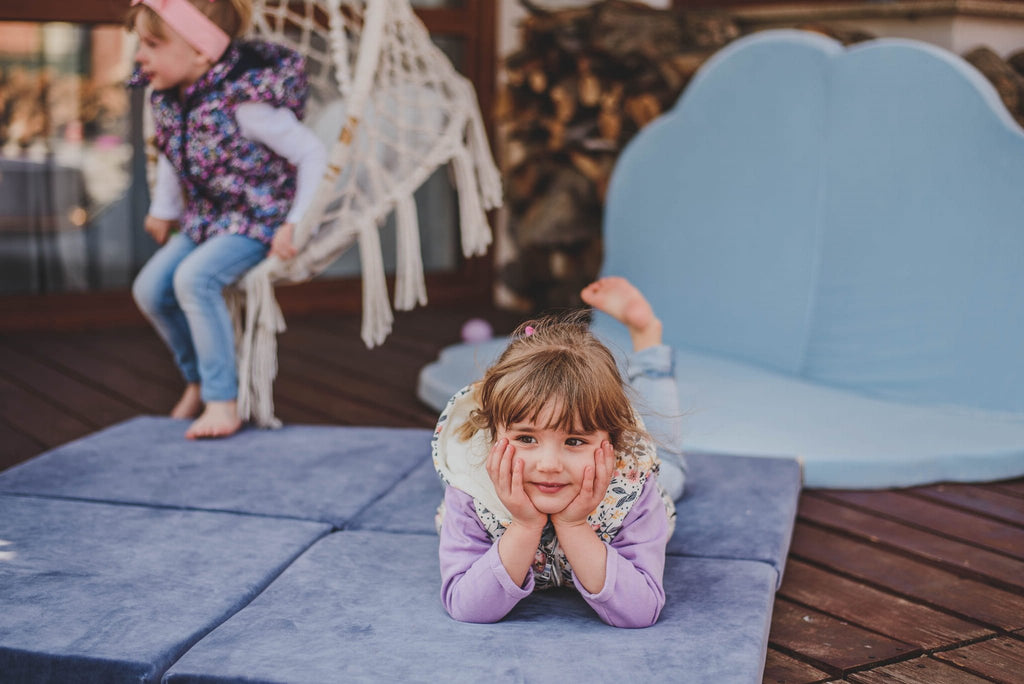 3. Two children playing on a blue-grey velvet play mat outdoors, one lying down and smiling