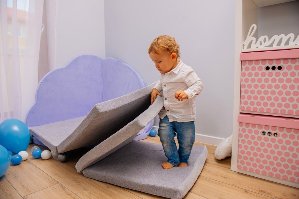 1. Toddler standing on folded light grey play mat in a playroom with blue and pink decor