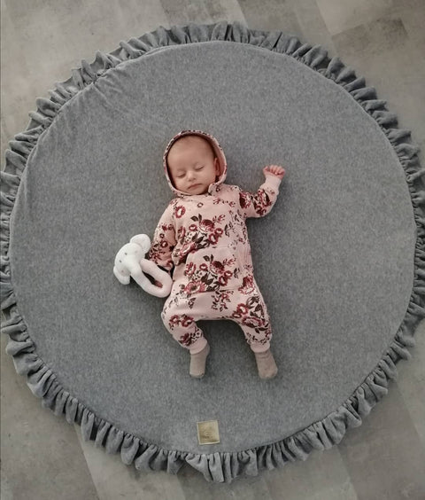 1. Baby sleeping on grey round play mat with frill, wearing floral outfit and holding white toy