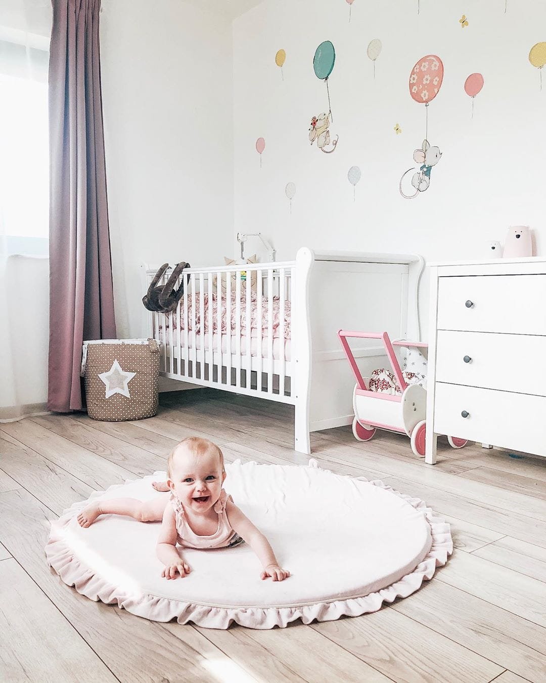1. Smiling baby on pink round play mat with frill in bright nursery with balloon wall art
