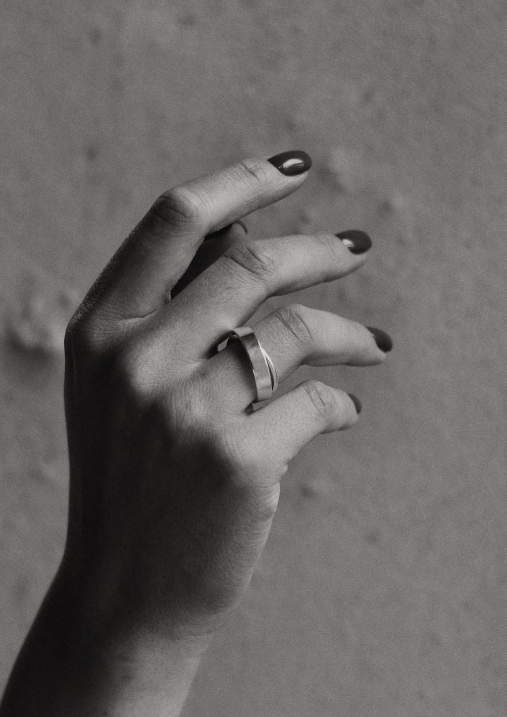 1. Black and white image of a woman's hand wearing the Milky Way ring by NO MORE, with a textured wall background