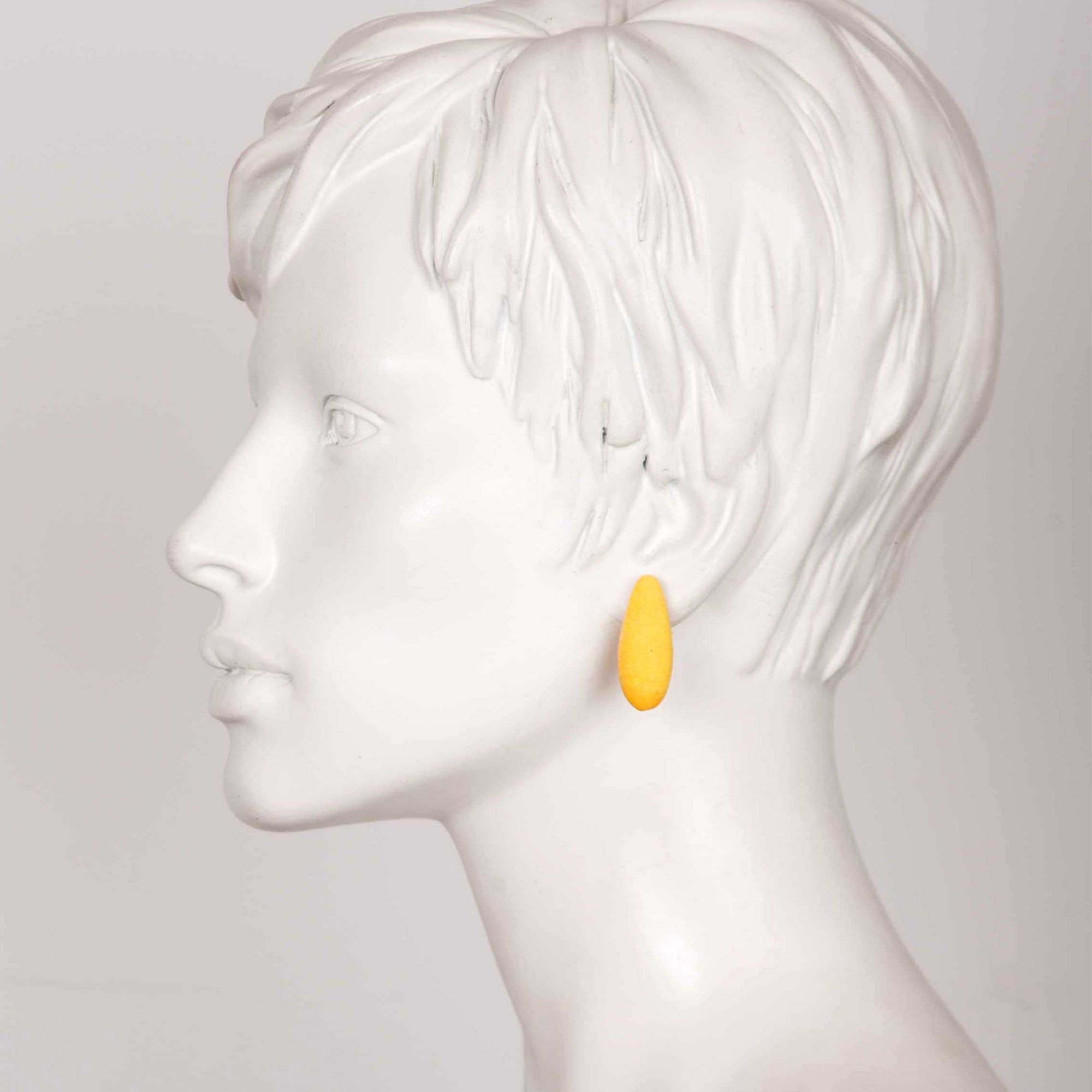 1. Side profile of a mannequin wearing Tanel Veenre Mini Bananas Earrings in yellow, highlighting the earring's length and vibrant color against a neutral background.