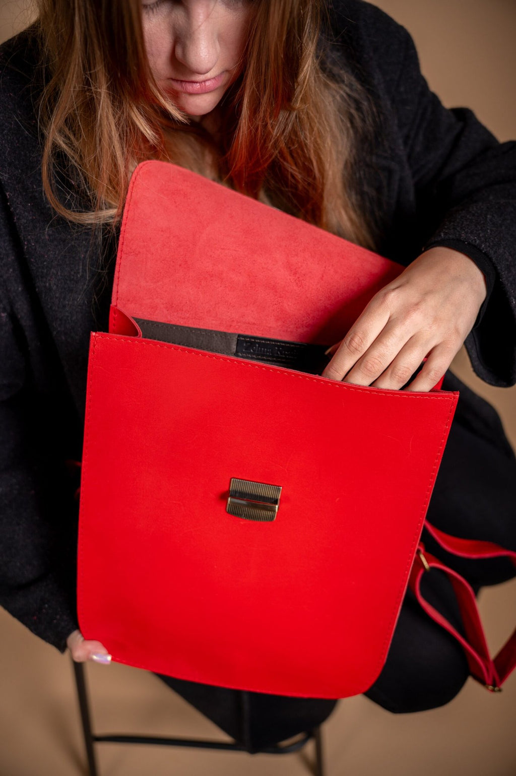3. Woman opening Zelma Kraft red leather saddle backpack, highlighting interior space and design