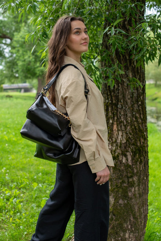 2. Woman wearing Zelma Kraft black leather hobo bag with gold chain over shoulder outdoors