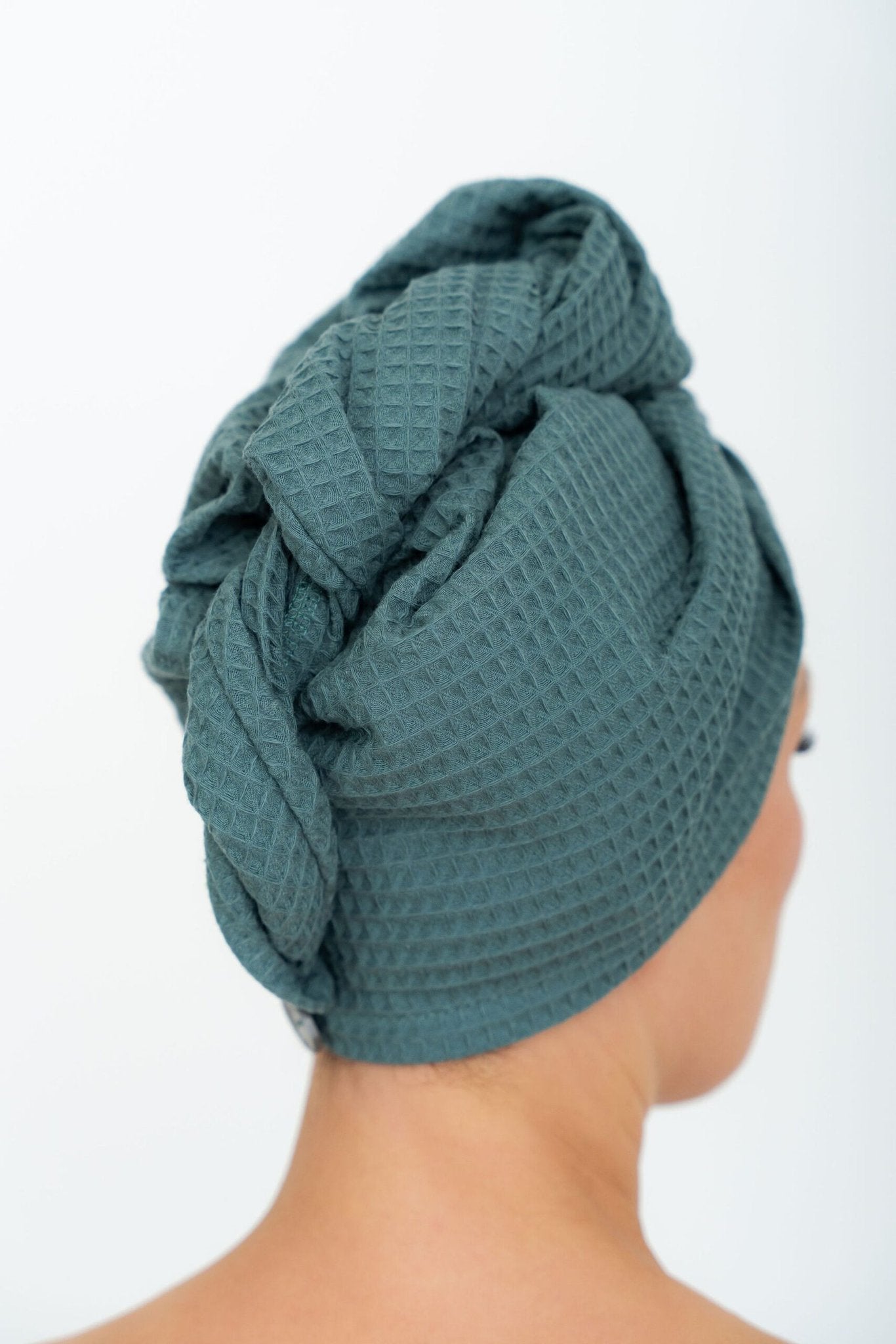 2. Back view of woman wearing petrol green cotton hair towel with button closure, highlighting texture