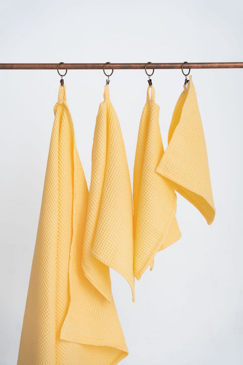 1. Set of four yellow organic waffle cotton towels hanging on a copper rod, showcasing different sizes with hanging loops