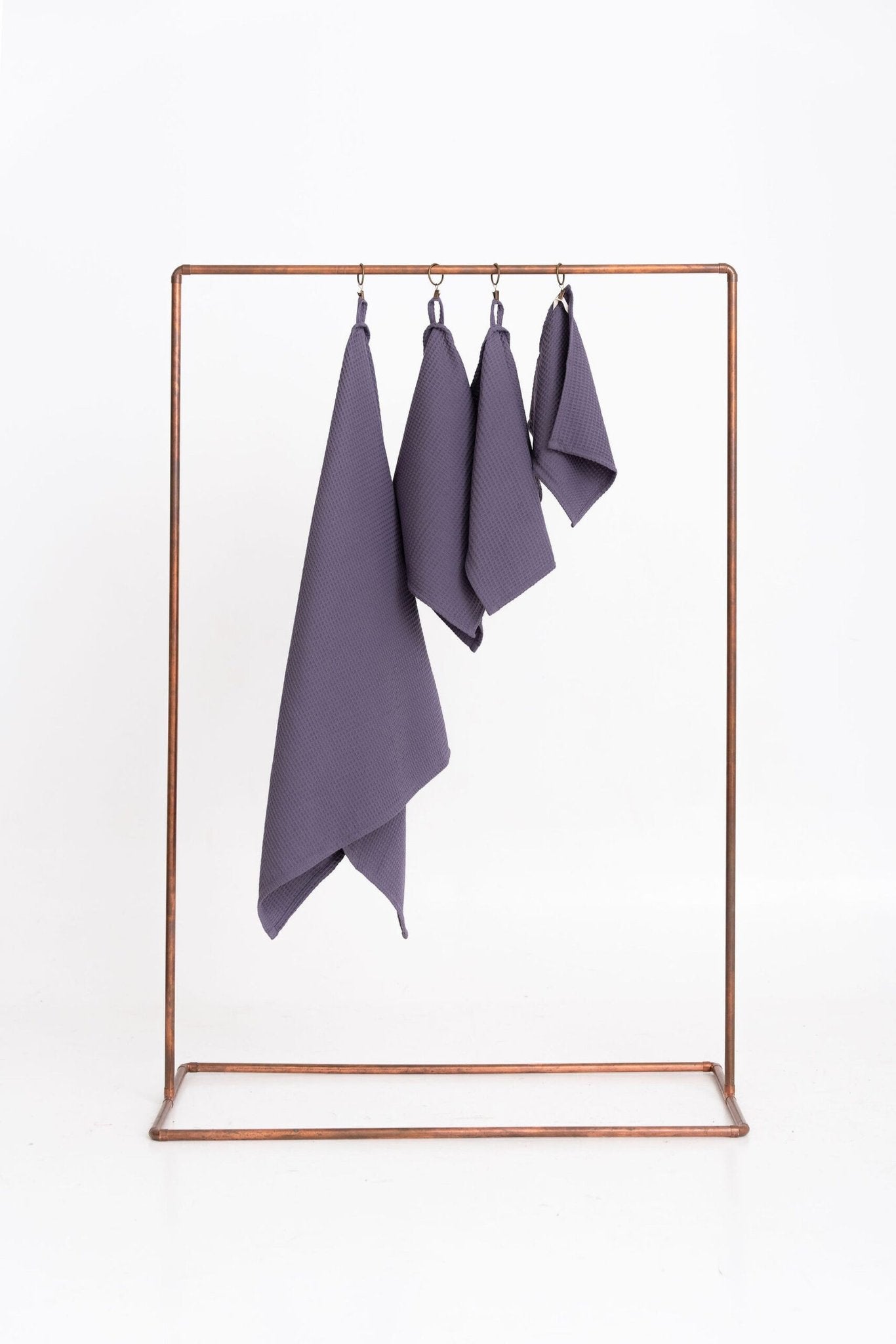 1. Set of four purple organic waffle cotton towels hanging on a metal rack against a white background