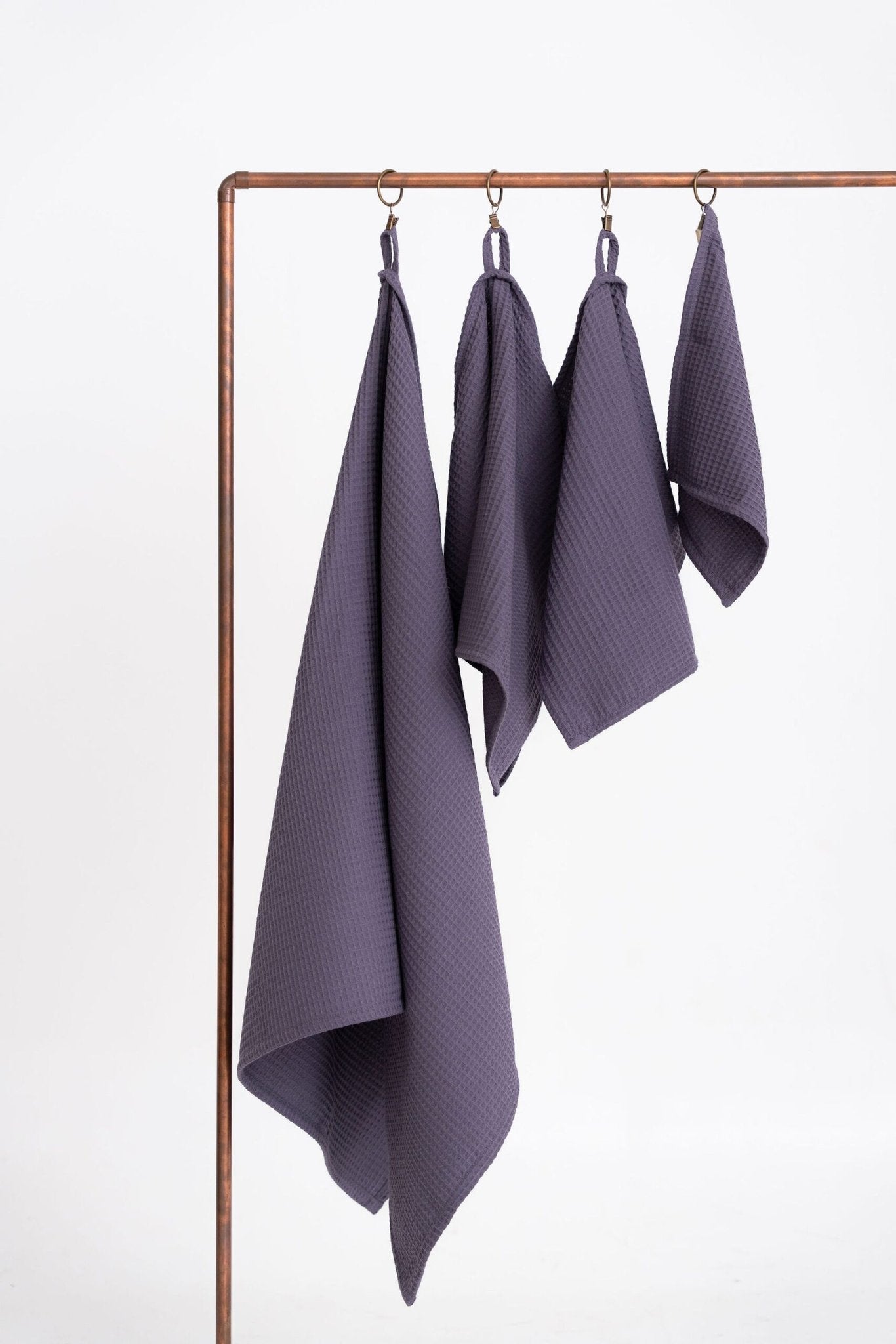2. Close-up of four purple waffle cotton towels by Nuss hanging on a copper rod