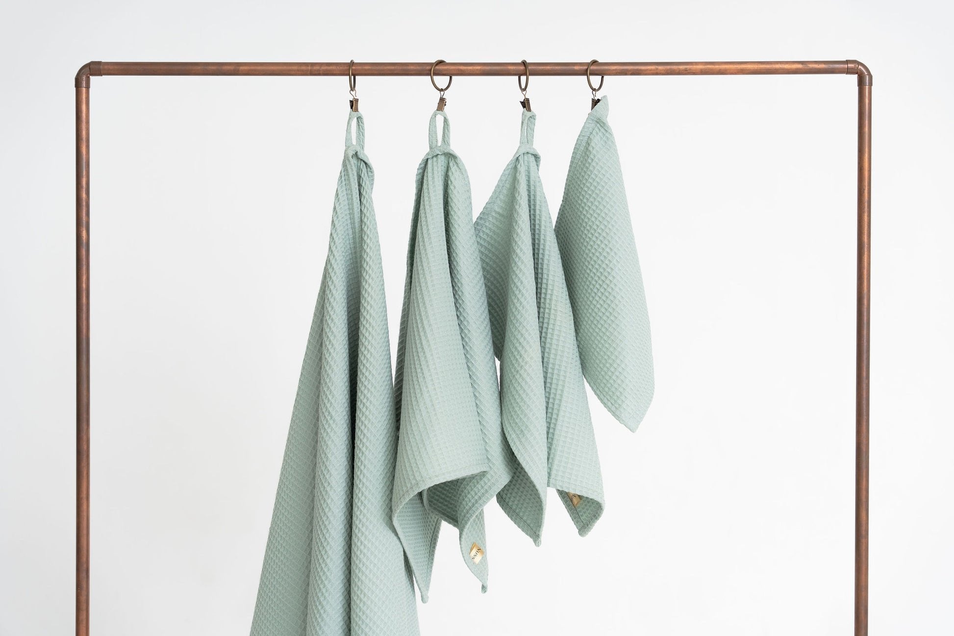 2. Studio shot of four sage green waffle cotton towels hanging on a metal rack