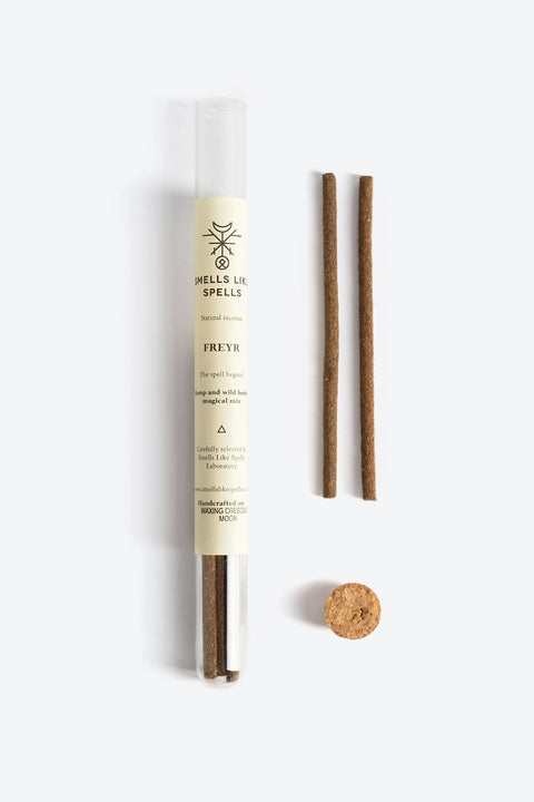 1. Flat lay of Smells Like Spells FREYR natural incense with two sticks, cork stopper, and green sprig on white background